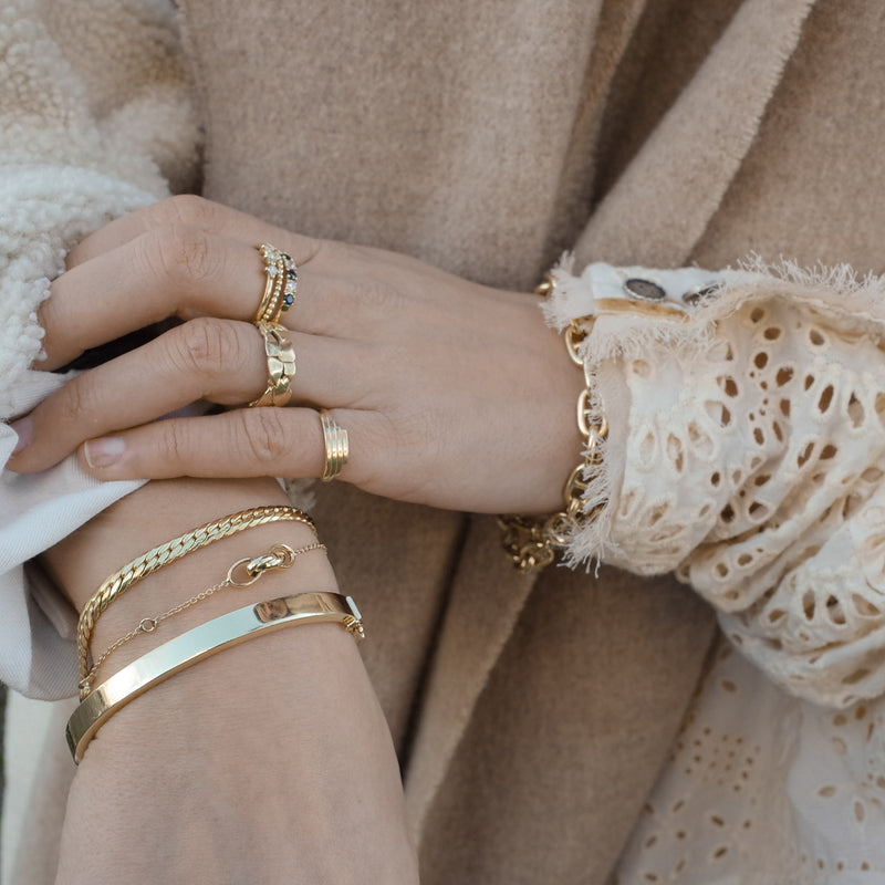Wrist with gold bracelets by Melanie Pigeaud, including the Snake bracelet 14k gold with a silver core. And a hand with rings