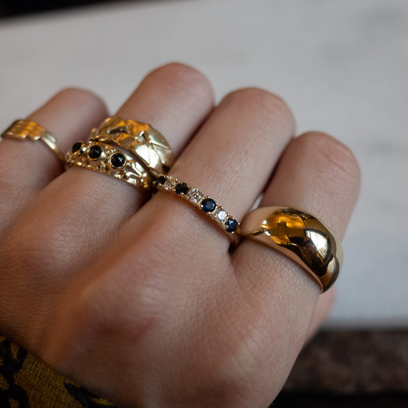 Hand with gold rings, including the Melanie Pigeaud sapphire zirconia row ring in 14 gold