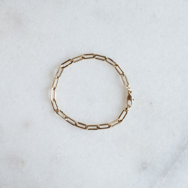 Drawn chain bracelet in 14k gold by Melanie Pigeaud presented on marble stone. 