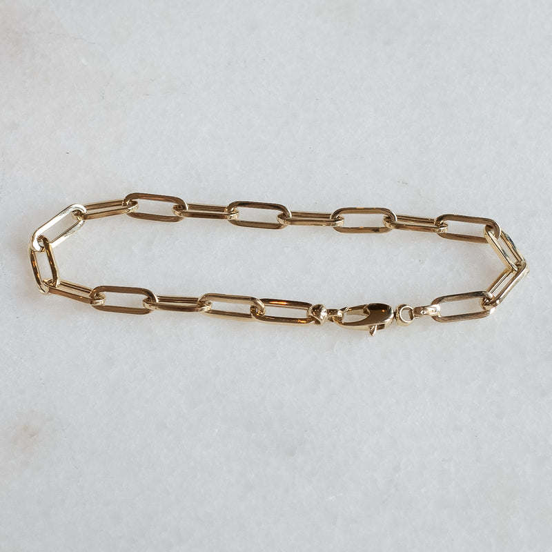 Drawn chain bracelet in 14k gold by Melanie Pigeaud presented on marble stone.