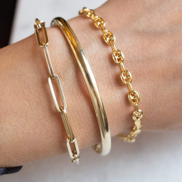 Wrist with three gold bracelets by Melanie Pigeaud, including the Coffee bean bracelet 14k gold