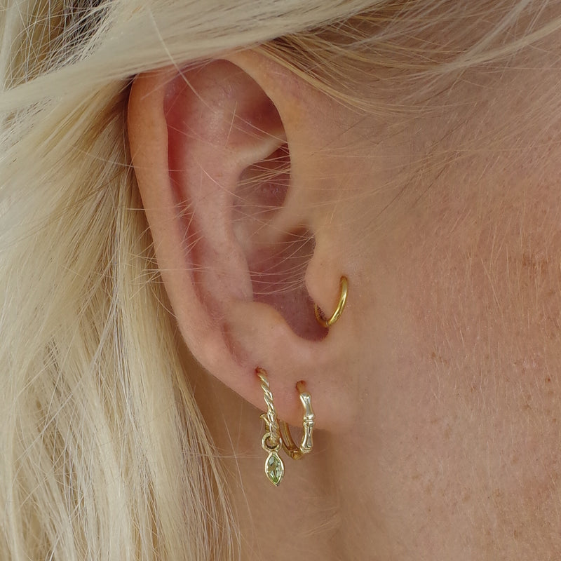 Ear with Melanie Pigeaud rope earring with peridot in 9k gold and Melanie Pigeaud bamboo hoop earring in 9k gold